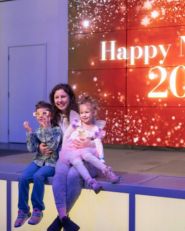Mother and two child smiling in front of Happy New Year screen