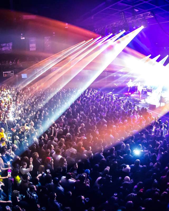 Concert with stage and bright, colorful stage lighting shining on large crowded audience