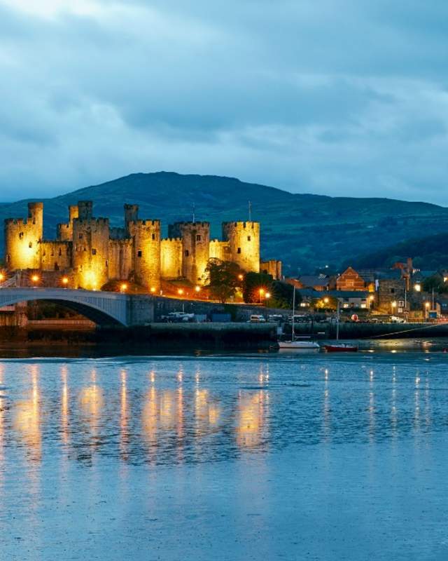 A view across the water of Conwy Castle at night, lit up