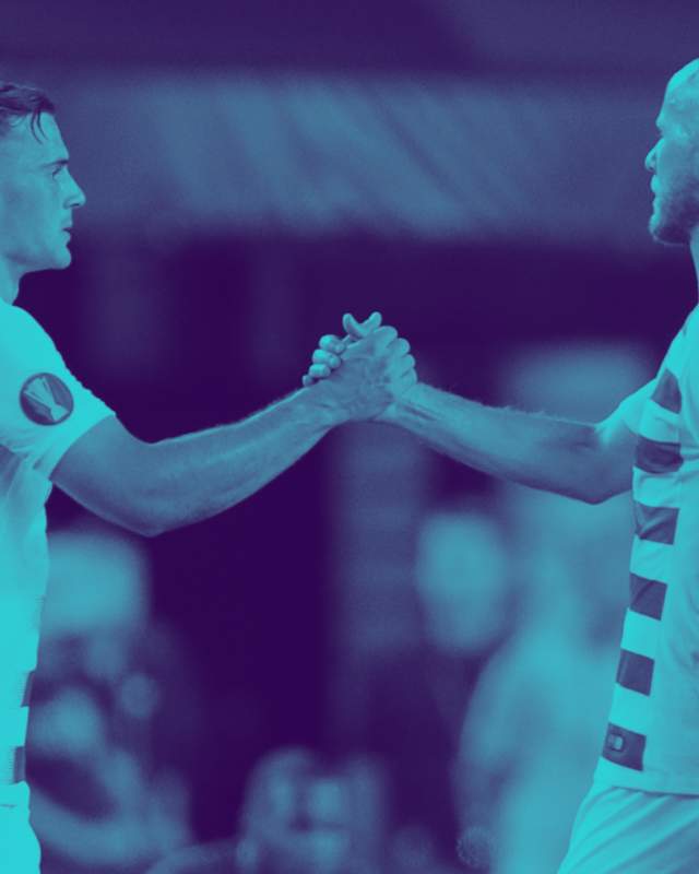 Two male soccer players shaking hands on a soccer field.