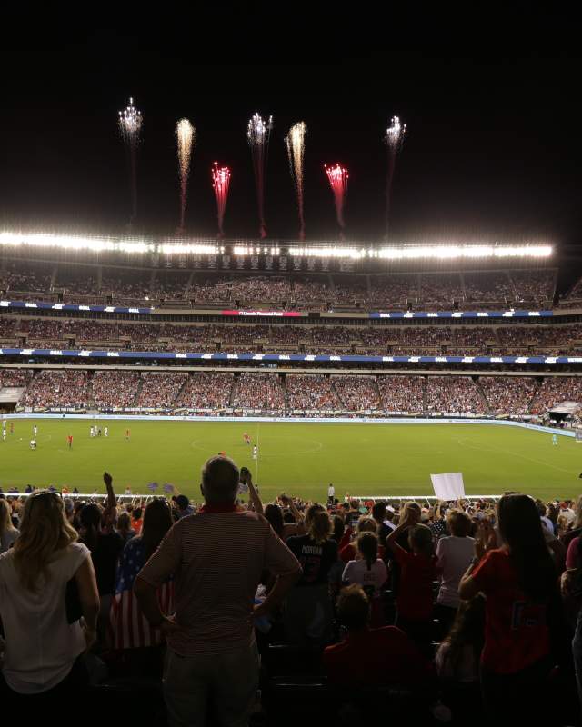 A view of a stadium from the stands, including fireworks flying into the sky.