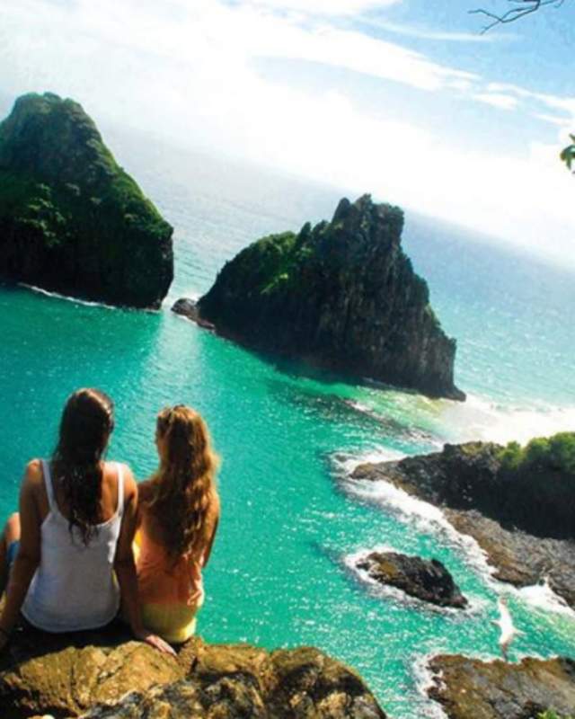 2 women sitting on a rock overlooking a beach