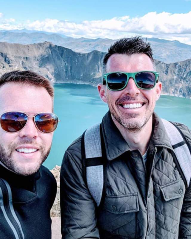 2 men in front of a lake with high peaks around it