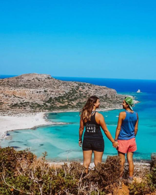 2 women standing on a hill overlooking a beach with a peninsula