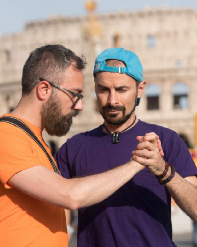 2 men holding hands in front of the colosseum