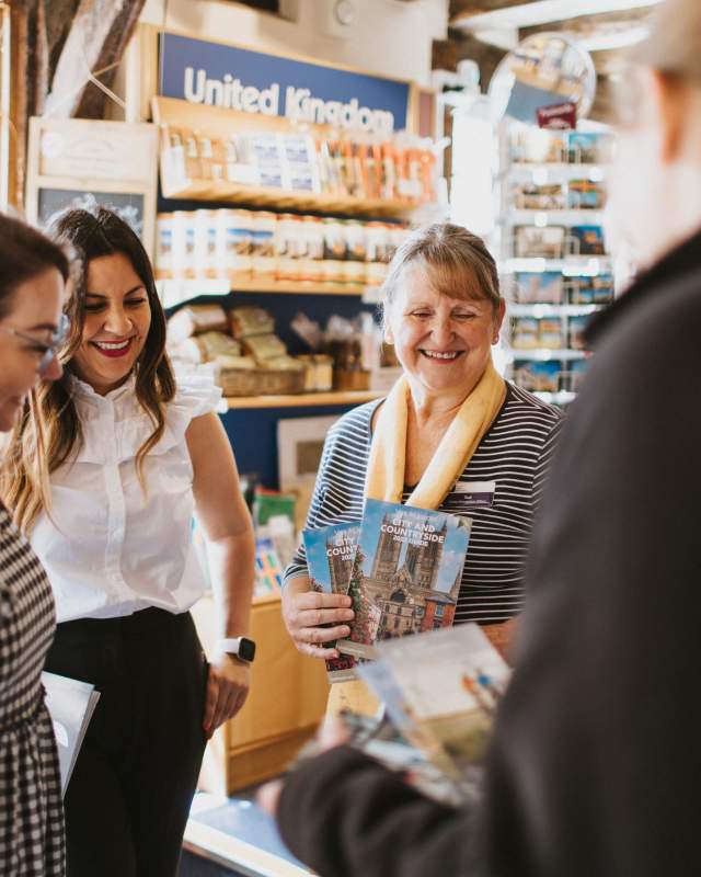 4 people stood in a group in a visitor information centre looking at leaflets