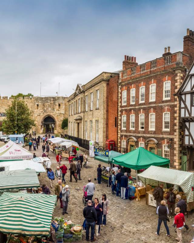 A farmers market outside of Lincoln Castle busy with stalls and people.