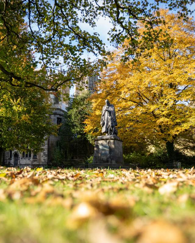 Alfred Tennyson statue surrounded by autumnal trees outside Lincoln Cathedral with blue skies