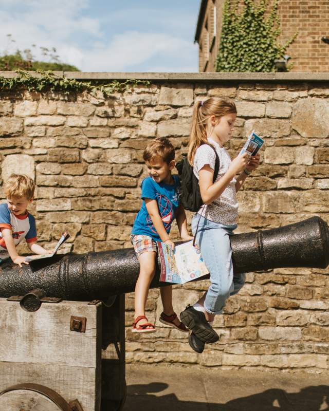 Three children sat on a castle cannon examining a guidebook