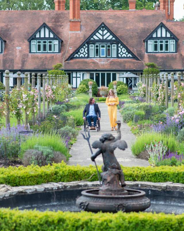 Man in wheelchair and woman walking in gardens outside Petwood Hotel