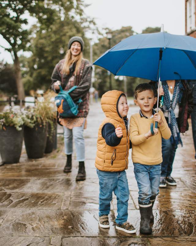 Two children standing under am umbrella in the rain with their parents behind them.