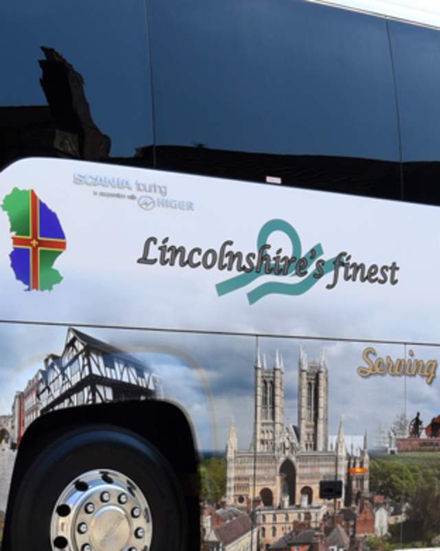 A side view of a PC Coaches Bus parked outside Lincoln Cathedral in the daylight