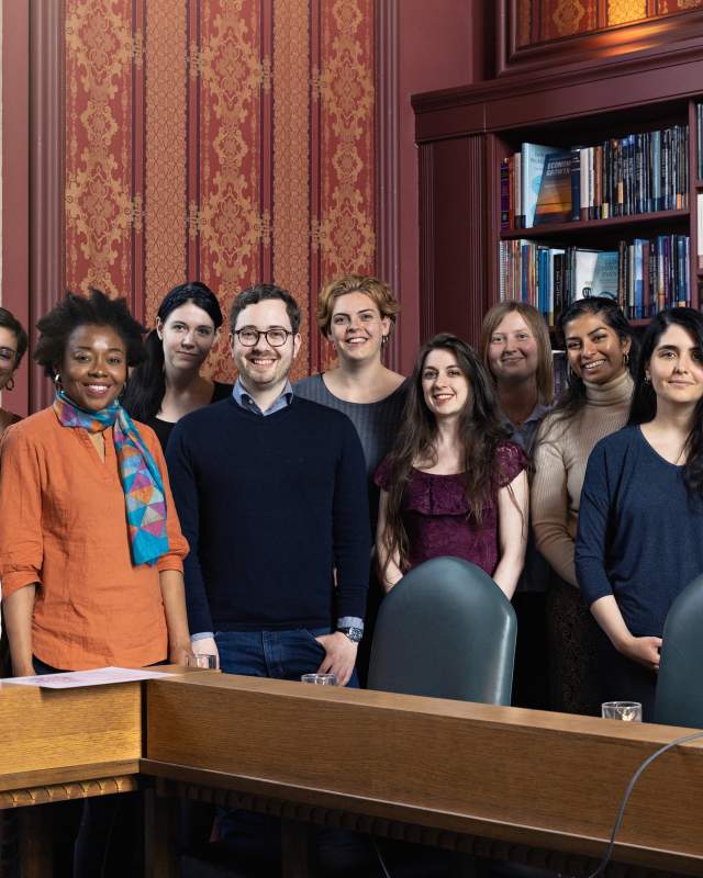 A group of mixed race men & women standing in front of a old wooden book case