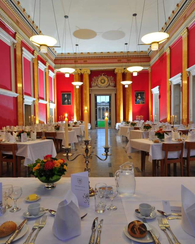 Downing College Cambridge dining hall: scarlet walls with a white ceiling. The hall is set up for formal dining with crisp white linen, candelabra, cutlery & fresh flowers