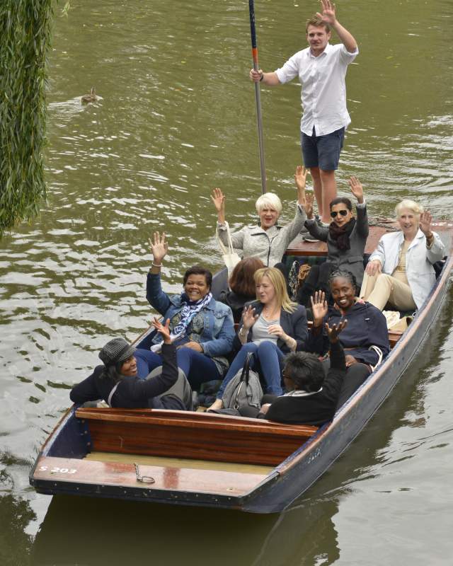 A group of people waving at the camera on a punt tour in Cambridge