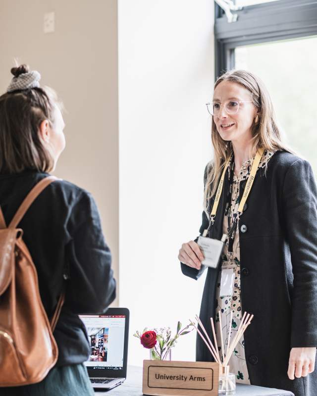 2 professional white women standing up and facing one another chatting about venues in Cambridge