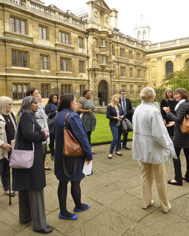 A group of people listening to a walking tour guide in the grounds of a Cambridge College