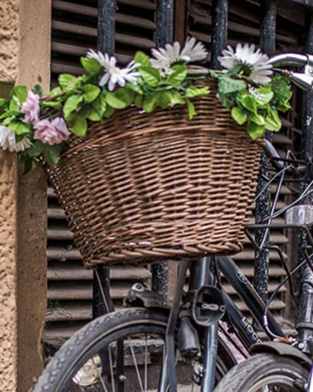 A pair of bicycles one with a basket of flowers against a wall in Cambridge.