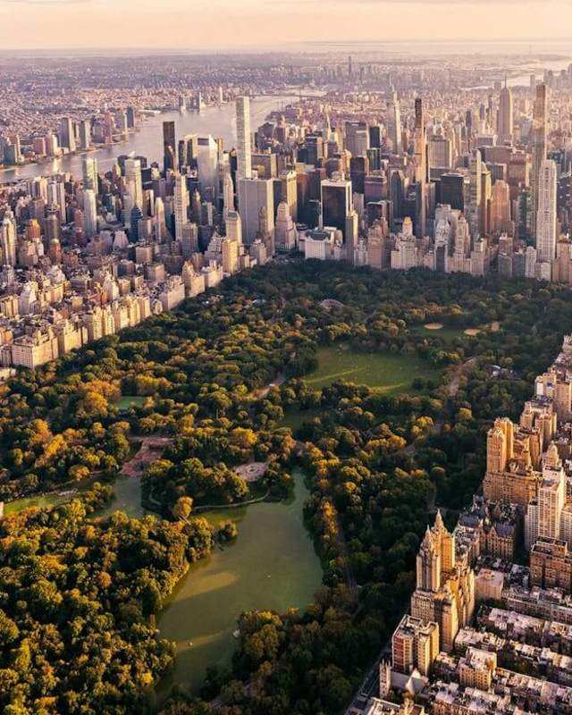 Golden-hour aerial view of Central Park's full expanse of autumn trees and The Lake surrounded by Manhattan skyscrapers, with Lower Manhattan visible in the distance