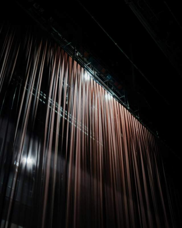 Closed stage curtain in a dark theater, matching the backstage Broadway theme