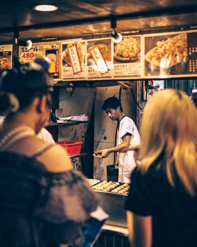 A vendor preparing food at a busy night market street stall with colorful dishes on display