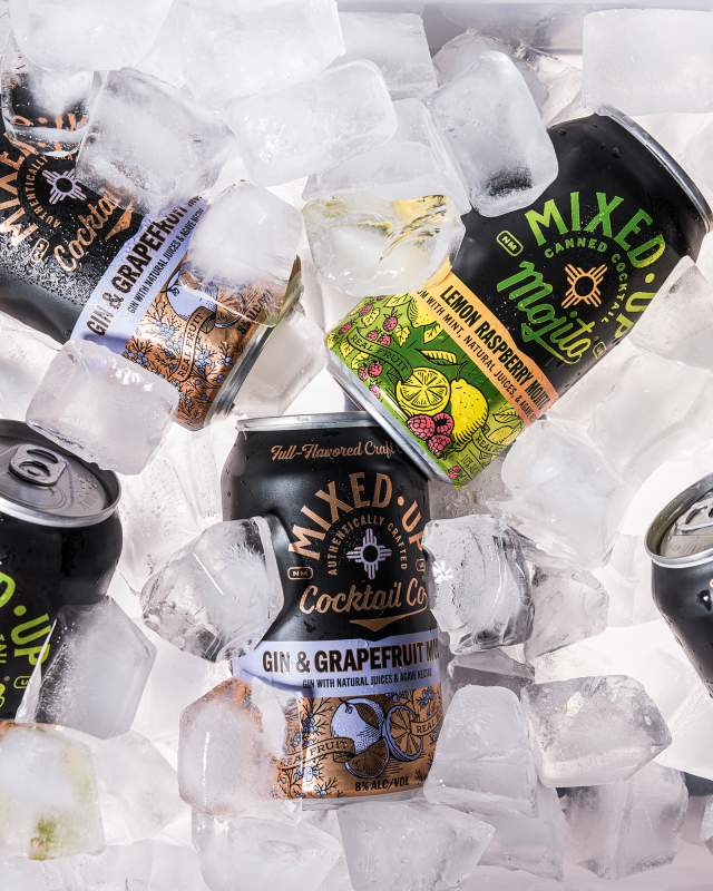 Cans of Mixed-Up canned cocktails scattered on ice.