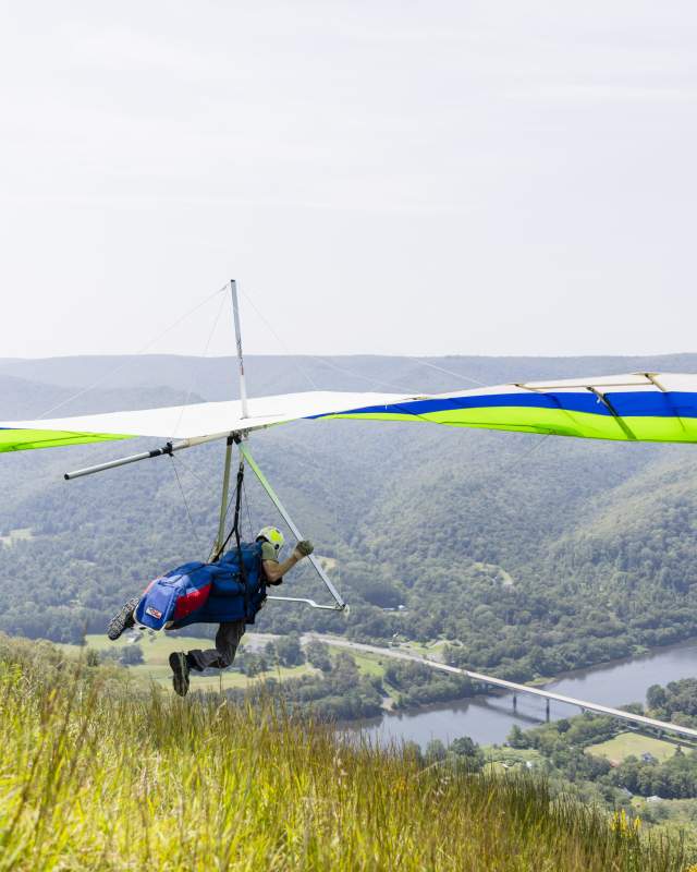 A person about to take off paragliding above a gorge with a river running through it.