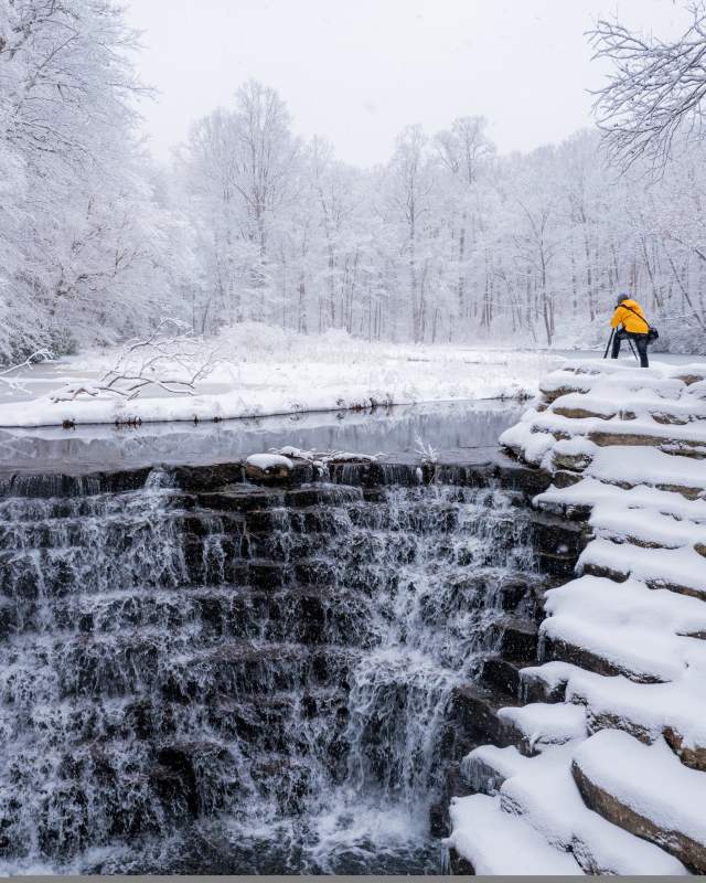 Man taking a picture with a camera on a snow covered waterfall in the Laurel Highlands