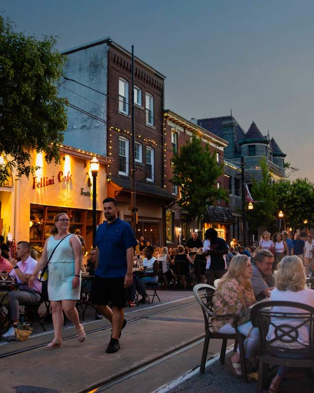 Crowds of people sitting at tables on a Main Street at dusk in the summer time