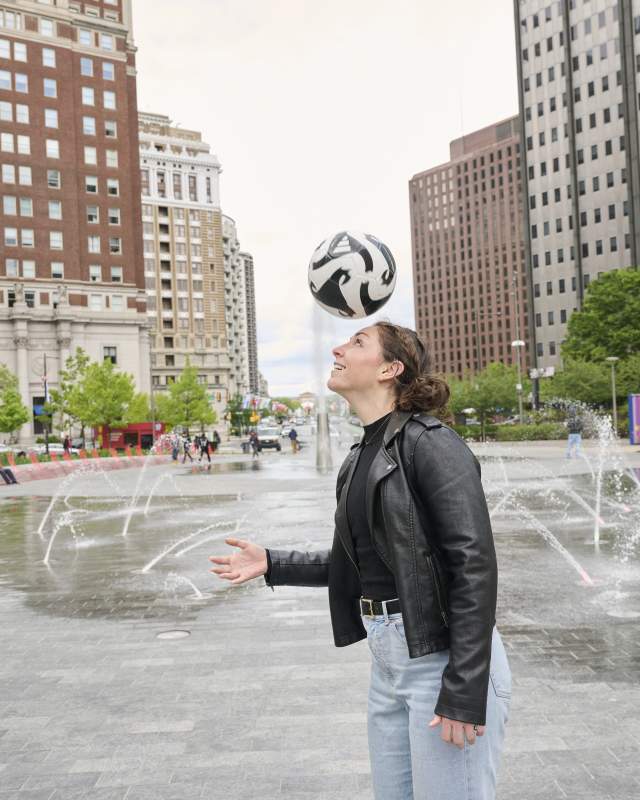 Woman in a leather jacket in LOVE Park in Philadelphia with a soccer ball hitting her head