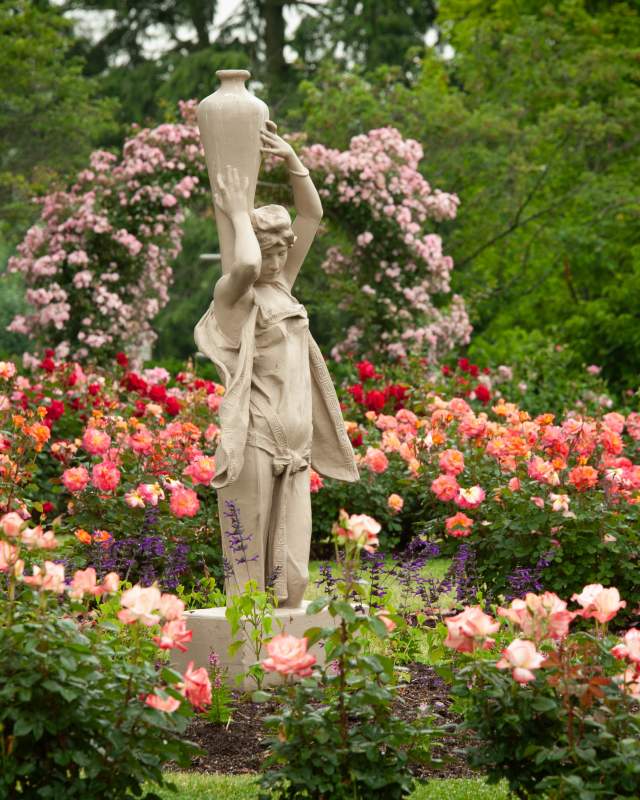 A sculpture in a garden surrounded by colorful pink, peach, and red flowers