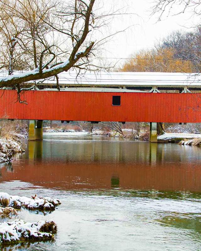 A red covered bridge over a river in the Lehigh Valley with snow on the ground