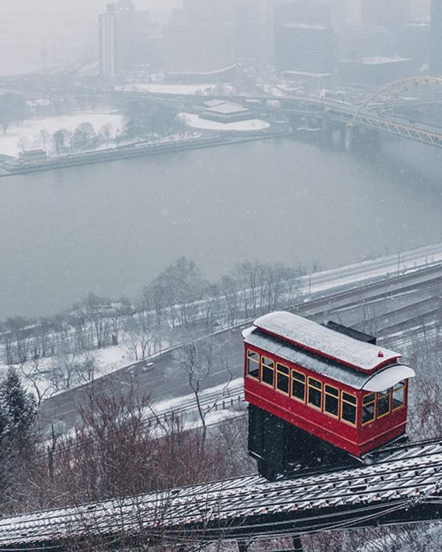 A red trolley car on the side of a hill making its way down the tracks with snow surrounding it