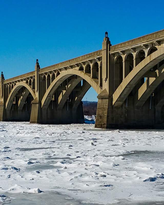 A frozen river with an arched bridge on a sunny day