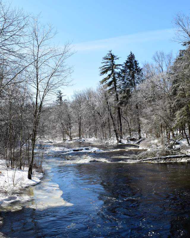A river flowing in a wooded area in the Pocono Mountains in winter with snow on the ground