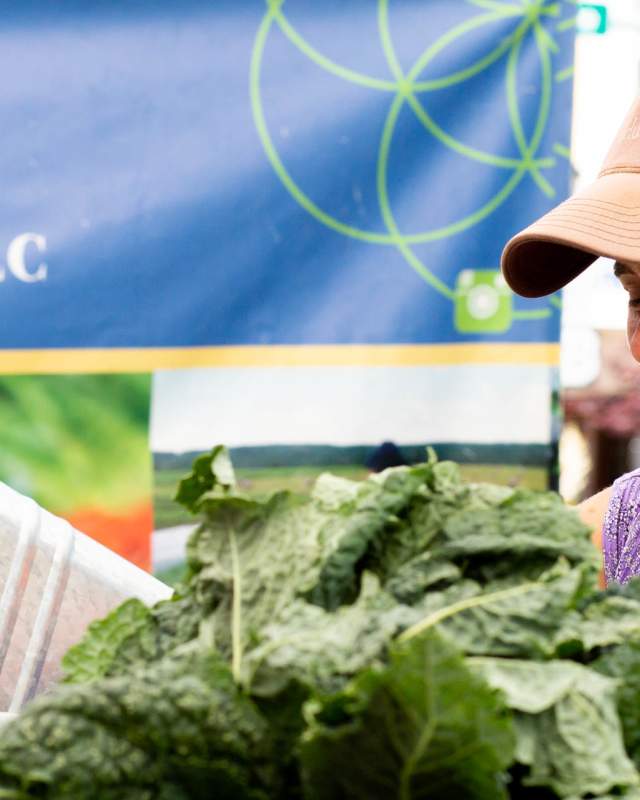 A woman smiles as she sells her organic produce at a farmers market