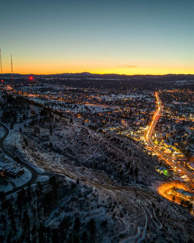 drone shot over city and skyline drive with sun setting and dusting of snow on Rapid City, SD