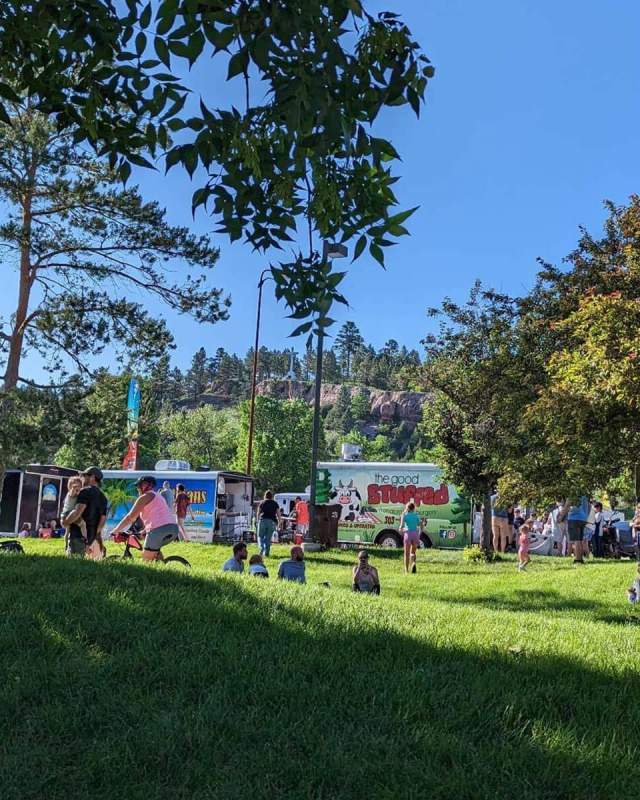 People scatter across the grass of canyon lake park with food trucks in the background