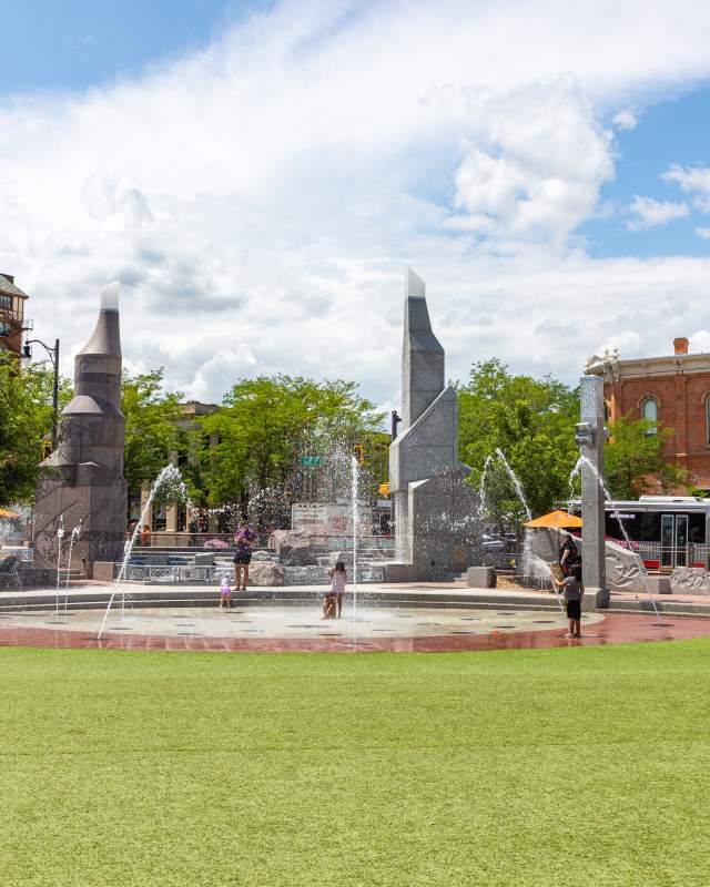 Green grass and an interactive splash patio surrounded by historic buildings in downtown Rapid City, SD.