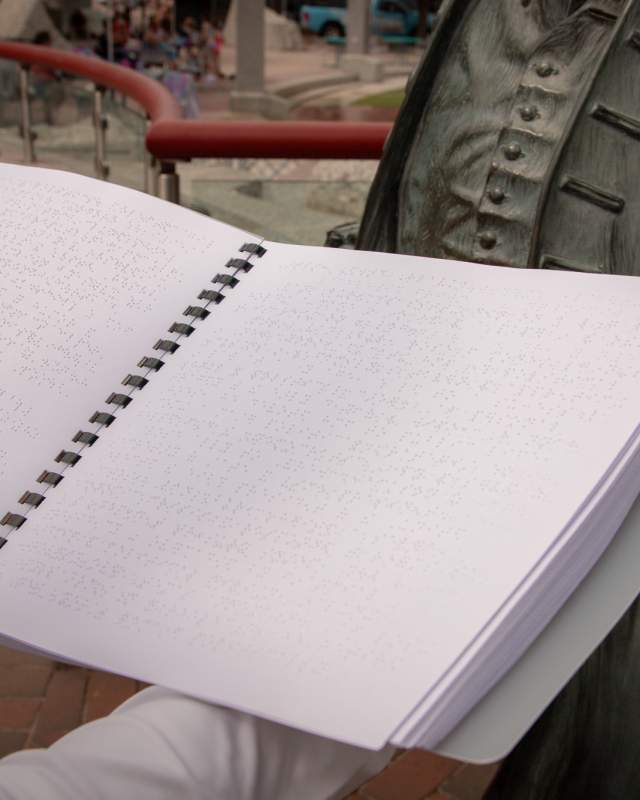 A woman holds the City of Presidents braille booklet in front of a bronze statue in Downtown Rapid City.