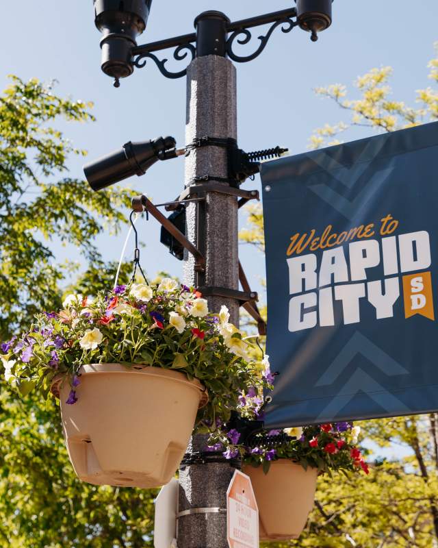Colorful flowers hanging on a flag pole with welcome sign in downtown rapid city, sd