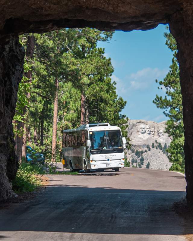 tour bus passing through the tunnel of iron mountain road with mount rushmore in the background