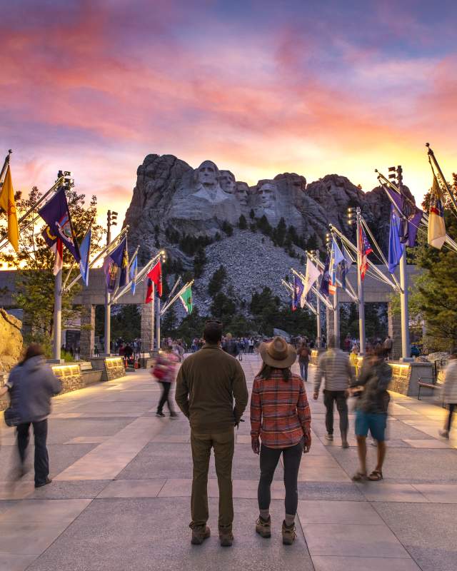 people standing on the avenue of flags at sunset at mount rushmore