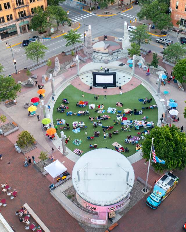 Aerial view of Movies on Main at Main Street Square, where attendees relax on blankets and lawn chairs around an outdoor movie screen in downtown Rapid City.