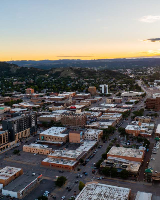Aerial view of downtown Rapid City at sunset with the Black Hills stretching across the horizon.