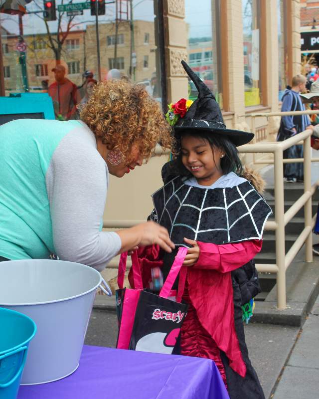 Child dressed in a witch costume collecting candy from a downtown business owner as part of the Downtown Trick-or-Treat event in Rapid City, SD.