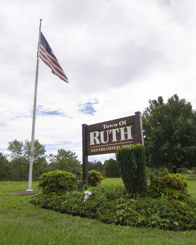 The welcome sign for Ruth, NC on a manicured green park with an American flag.