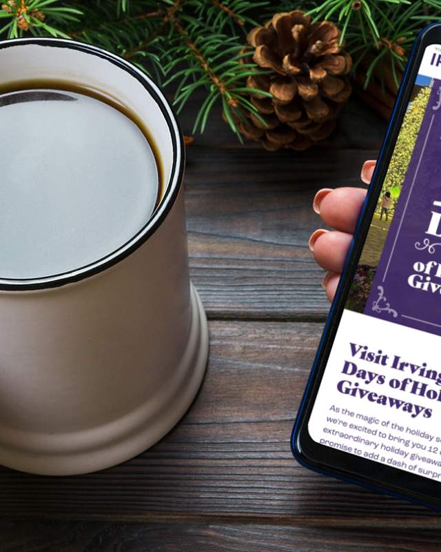 A person holds a mug of coffee in one hand and a mobile phone open to a webpage showcasing Irving's 12 days of holiday giveaways open in the other.