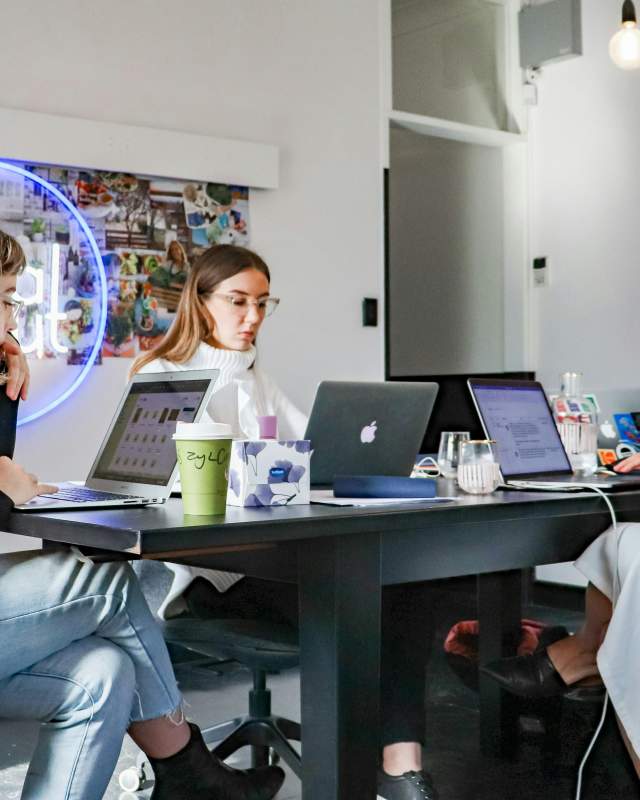 Three women work on their laptops while seated at the same table.
