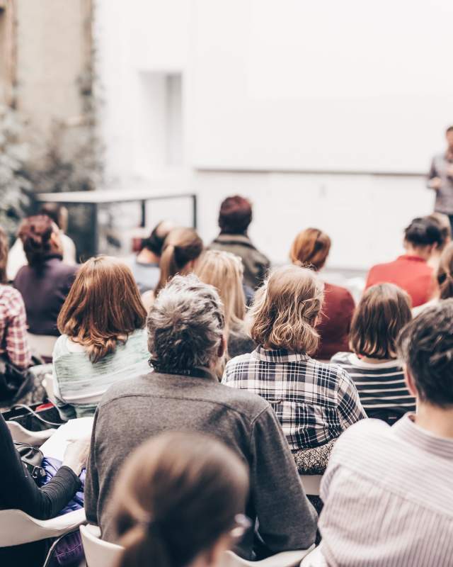 A person giving a presentation as people sit closely in a small meeting room.